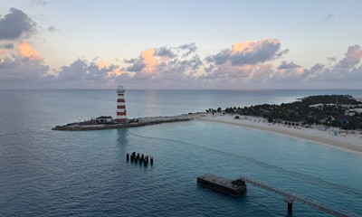 Aerial view of Ocean Cay with its iconic red-and-white striped lighthouse, sandy beach, and calm turquoise waters at sunrise.